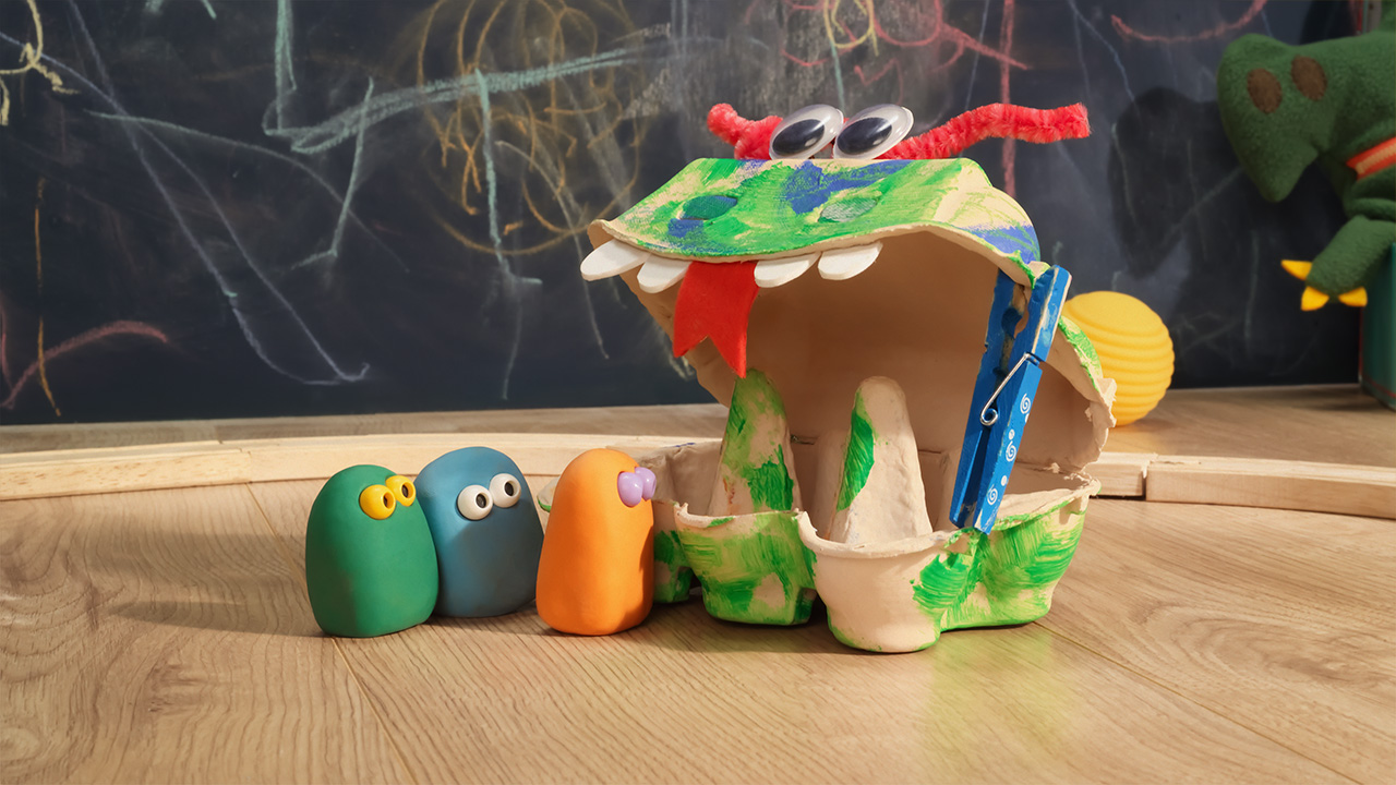 Green, Blue and Orange are looking into the mouth of a monster made from an egg box 
